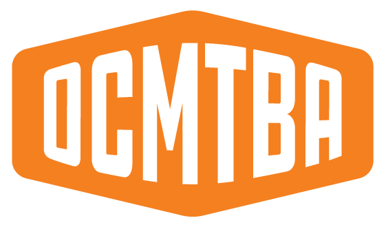 OCMTBA logo - a drawing of an orange with a bike and the initials OCMTBA inside.